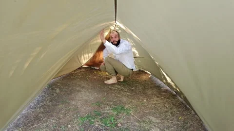 Man adjusting ridgeline inside camping tarp shelter in woods Stock Footage 344894057