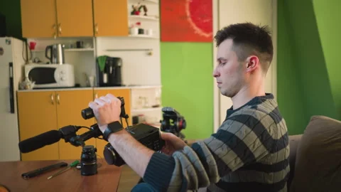 Man adjusting tripod-mounted camera with microphone in home studio Video stock 317588212