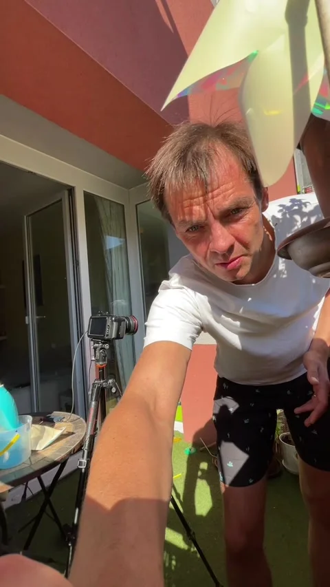 Man adjusts camera on sunny residential balcony reaching toward lens with Stock Footage 344881728
