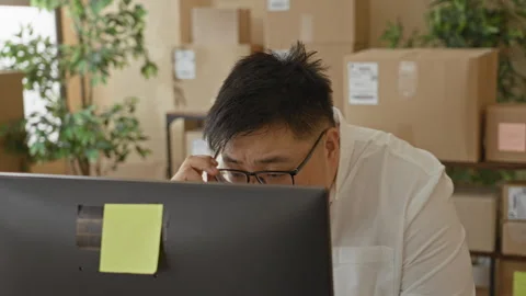 Man adjusts glasses while checking parcels at computer in building; small b.. Stock Footage 337390408