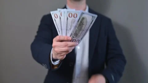 A man adjusts his clothing while holding stacks of cash in both hands. The Stock Footage 338299972