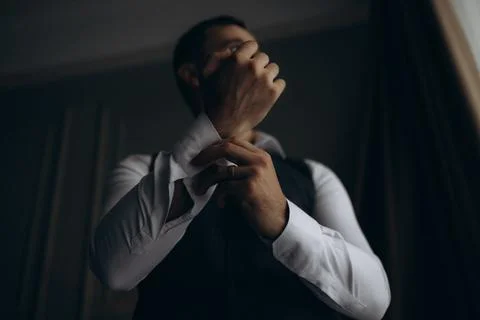 Man adjusts his cuff in dim, intimate lighting Foto stock