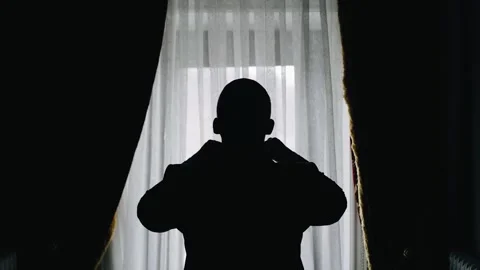 A man adjusts his jacket and tie standing in front of a bright window Stock Footage 281016829