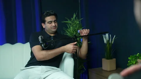 Man Adjusts Microphone While Hosting Podcast Conversation in Modern Studio Видео 337436931