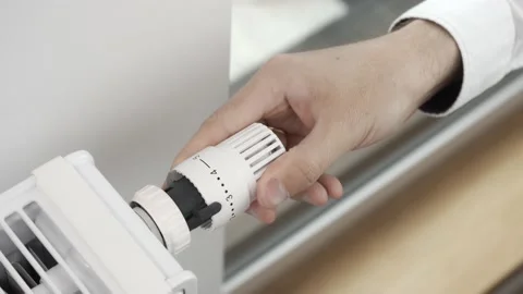 The man adjusts the radiator thermostat to the maximum temperature in the room 库存影片 211621292