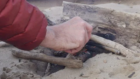 Man Adjusts Small Drift Wood Fire On Sandy Beach Stock Footage 344911595