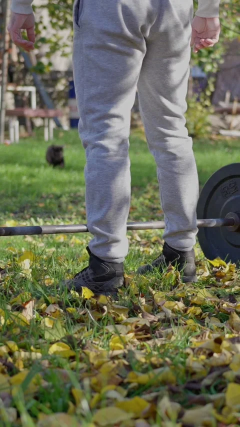 Man adjusts stance on grass, individual in gray tracksuit readying to lift Video stock 321612277