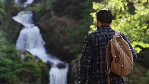 Man admires a mountain landscape and a waterfall during a hike. Stock Footage 254916640