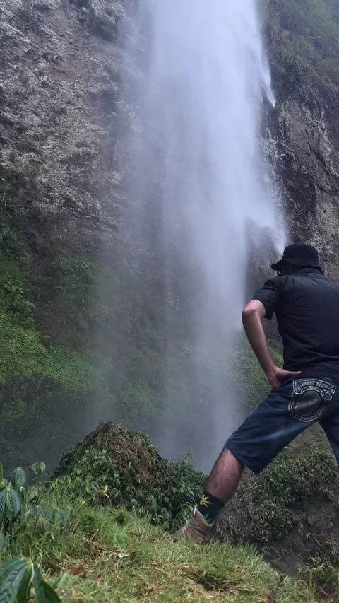 Man Admiring Large Waterfall, Mossy Cliff, Vertical Shot Stock Footage 323912461