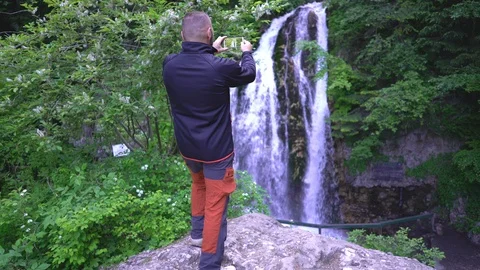 Man admiring the waterfall and doing photos on smartphone Stock Footage 103506804