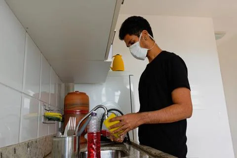 Man adult black wearing coronavirus  mask washing dishe in kitchen Stock Photos