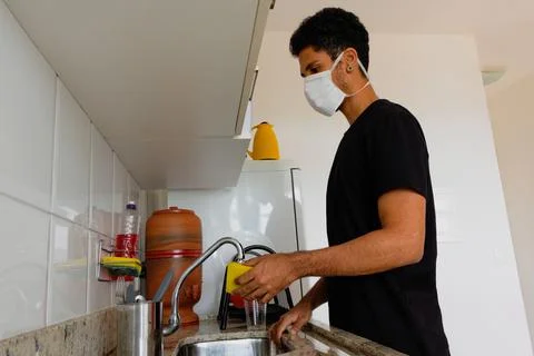 Man adult black wearing coronavirus  mask washing dishe in kitchen Stock Photos