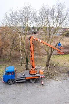 Man on aerial platform pruning branches of tree with chainsaw Stock Photos