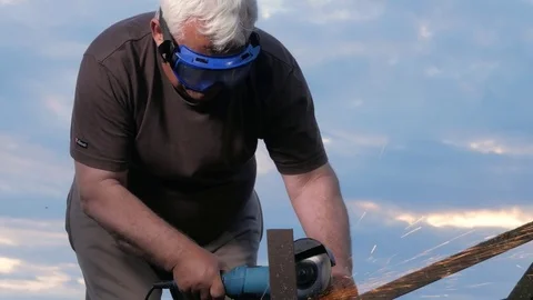 A man in age cuts off a metal angle grinder at sunset. Beautiful sky behind the Stock Footage 76917567
