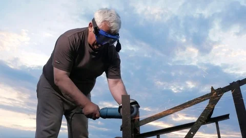 A man in age cuts off a metal angle grinder at sunset. Beautiful sky behind the Stock Footage 76917655