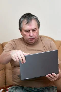 A man at the age of sitting on Devani looks through the news on a laptop. Stock Photos
