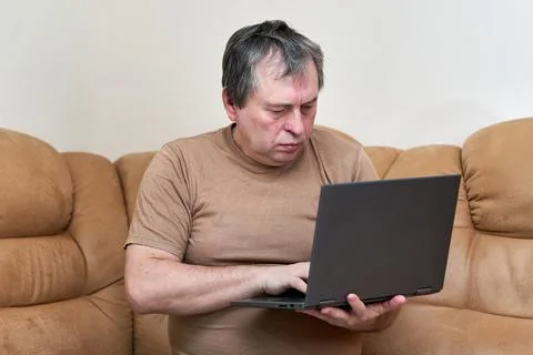 A man at the age of sitting on Devani looks through the news on a laptop. Stock Photos