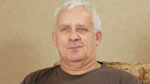 The man at the age of sitting at home on the couch and looking toward the camera Stock Footage 71244516