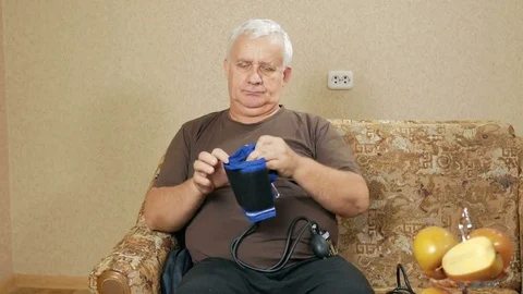 Man aged overweight measures the pressure of their own home on the couch. He Stock Footage 71245565