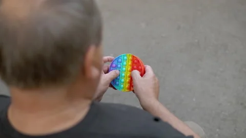 A man aged plays in a popit on the background of a public park. The person is Stock Footage 159650148