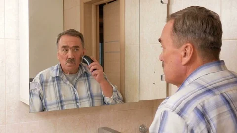 Man aged shave electric razor in the bathroom. He looks in the mirror and Stock Footage 70134452