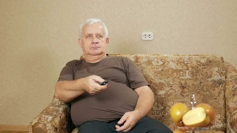 Man aged switches remote control TV channels on the couch at home. He relaxes Stock Footage 71245146