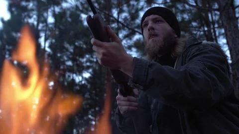 Man aiming a gun in front of a campfire at danw Stock Footage 76476807