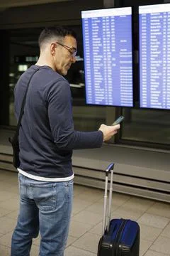 Man at airport in front of timetable using smartphone Stock Photos