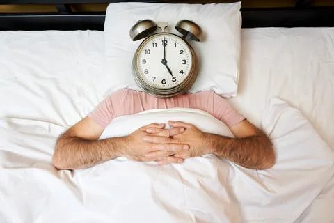 Man with alarm clock instead of head lying in bed. Morning concept Stock Photos
