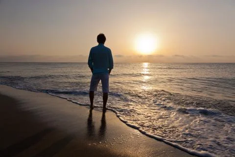 Man alone on beach watching the sunset Stock Photos