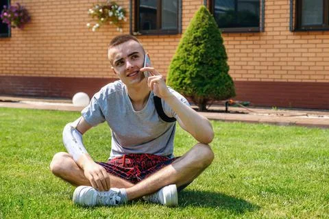 Man with amputated arm and prosthesis talking on the phone sitting on the lawn Stock Photos