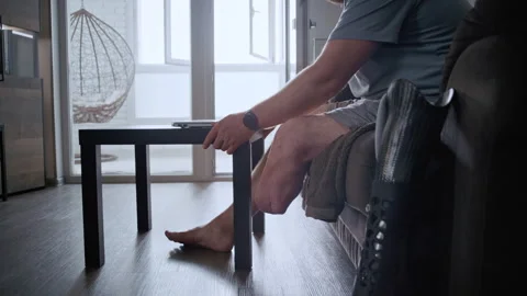 Man with Amputated Leg Putting on Prosthesis in Living Room Stockbeeldmateriaal 317974471