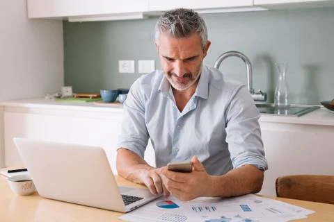 Man analysing data and using laptop and cell phone in home office Foto stock