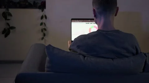 Man analyzing charts on laptop while sitting on sofa in cozy home environment Stock Footage 314550949