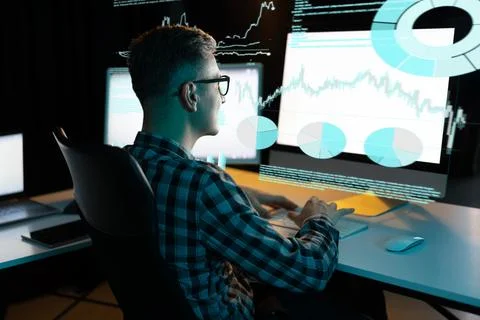 Man Analyzing Data Graphs on Multiple Computer Screens in Modern Office 写真素材