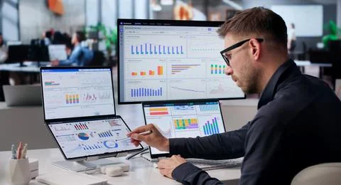 Man Analyzing Financial Data On Dual Screens In Modern Office Space. Stock Photos