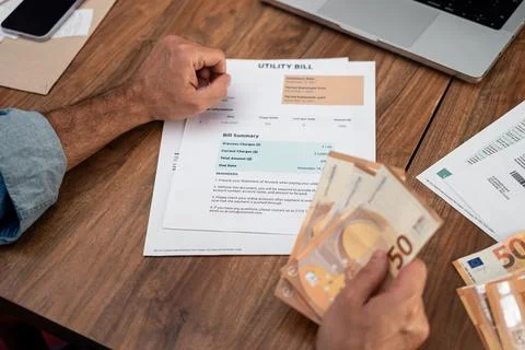 Man analyzing utility bill while holding euro banknotes at home. Focus on Foto stock