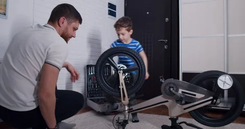 A man and a boy bond while fixing a bicycle in a cozy living room Stock Footage 307296178