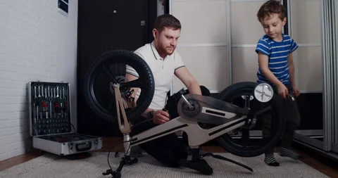 A man and a boy bond while fixing a bicycle in a cozy room Stock Footage 307296262