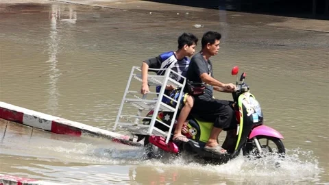 A man and a boy carry a load on a motorbike through a flooded street Video stock 220822856