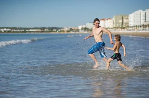 The man and the boy joyfully run in to swim in the sea. Stock Photos