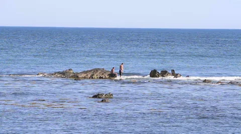 Man and boy playing on rocks in the ocean Stock Footage 33824495