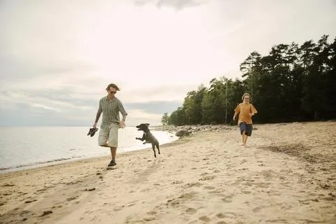 Man and Boy Running with Jumping Dog on Sandy Beach Coast Stock Photos