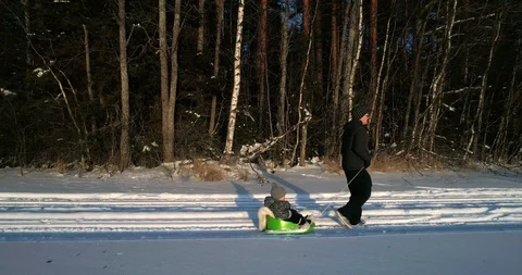 Man and a boy sledding , Cinema 4k aerial view away from a father draging a k Stock Footage 87630645