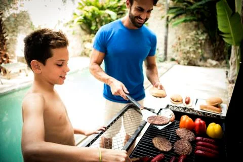 A man and boy standing at a barbecue cooking food. Stock Photos