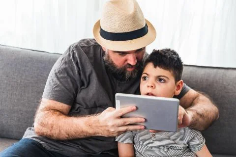 Man and boy with a tablet on the sofa of a house Stock Photos