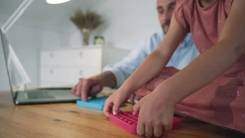 A man and a child are playing Poppit. A man working at a laptop takes a break Stock Footage 156792995