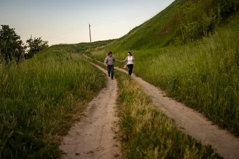 A man and a girl in rustic clothes run along a village road Stock Photos
