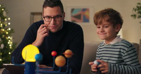 A man and his son assemble a planetary model during Christmas evening. They 库存影片 210472919