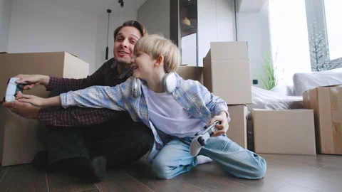 A man and his son sit on the floor and play video games in their new house Stock Footage 346225872
